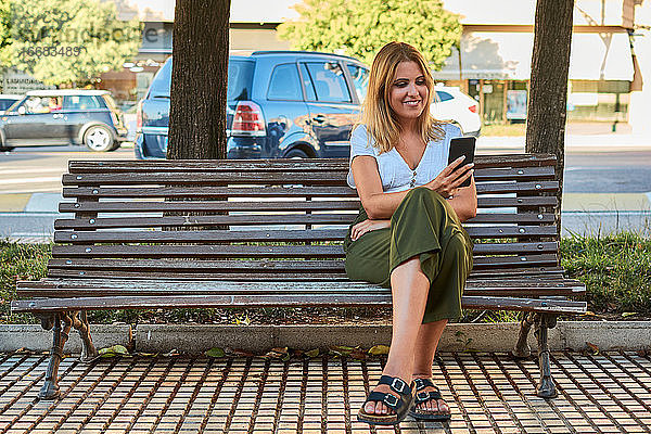 Junge Frau schaut auf ihr Telefon  während sie auf einer Bank sitzt