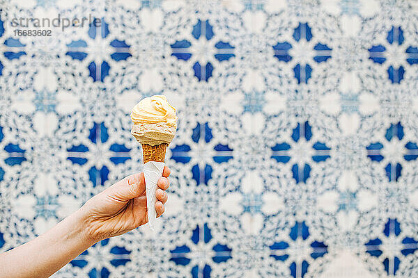 Weibliche Hand hält Eiswaffel auf unscharfem weiß-blauem Hintergrund