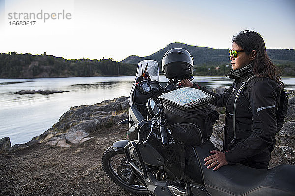 Frau steht neben einem Tourenmotorrad am Lago Alumine in Argentinien