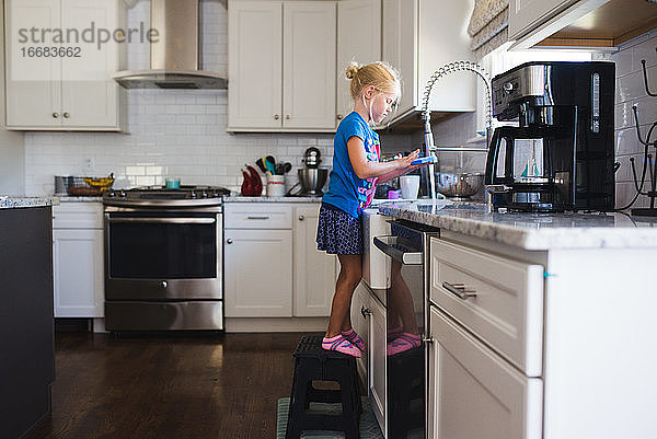Kleines Mädchen am Spülbecken beim Geschirrspülen