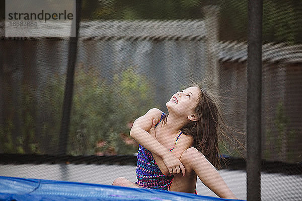 Ein lachendes Kind mit wilden Haaren spielt auf einem Trampolin in ihrem Garten