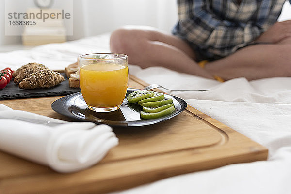 Nahaufnahme von Frauenbeinen und einem Frühstückstablett mit Obst auf einem Bett.