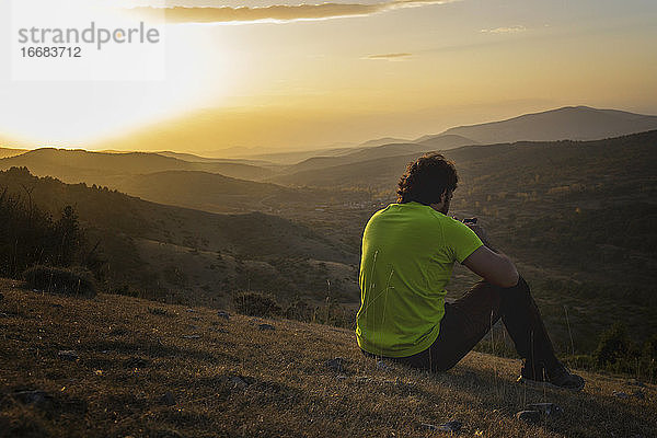 Mann schaut bei Sonnenuntergang auf dem Gipfel eines Berges auf sein Smartphone