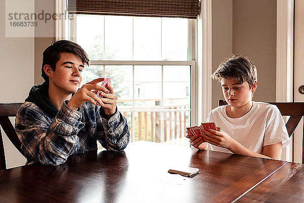Zwei Teenager spielen zusammen am Küchentisch Karten.