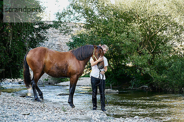 Porträt eines jungen blonden Mannes  der auf einem Pferd über einen Fluss reitet