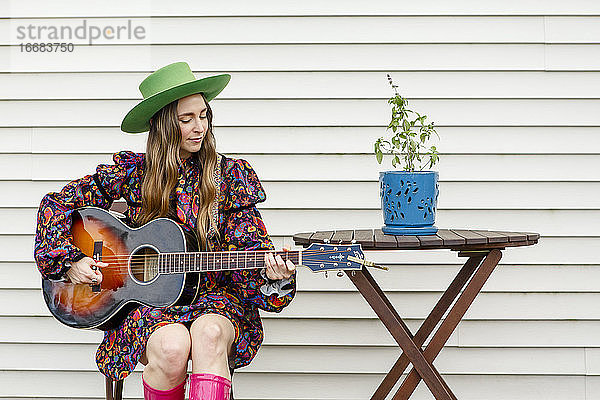 Eine schöne Frau sitzt an einem Tisch im Freien und spielt eine akustische Gitarre