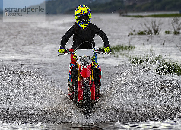 Frau fährt mit ihrem Dirt-Bike durch einen See bei Pak Chong / Thailand