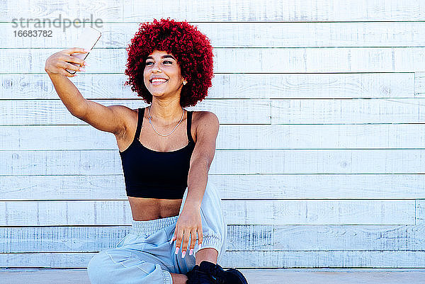 Frau mit rotem Afro-Haar macht ein Selfie mit Handy.