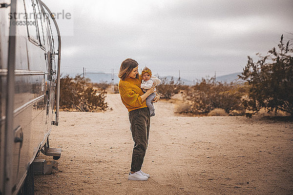 Eine Frau mit einem Baby steht in der Nähe eines Wohnmobil-Anhängers  Joshua Tree  Kalifornien