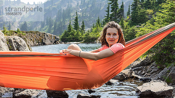 Frau entspannt sich in einer Hängematte am Alpensee im Urlaub vor Ort