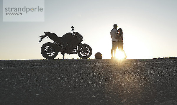 Gegenlicht eines Paares  das mit seinem Motorrad auf der Straße posiert