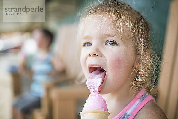 Junges süßes Mädchen leckt fröhlich rosa Eis am Sommertag.
