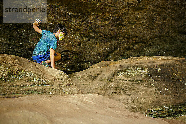Ein Junge krabbelt über Felsbrocken gegen eine Felswand in einer Sandsteinschlucht
