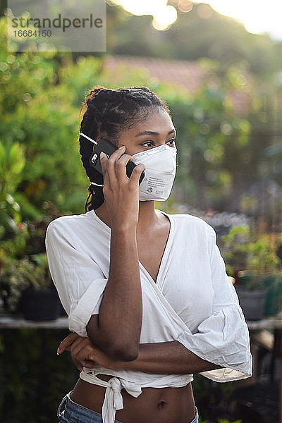 Junge schwarze Frau mit Gesichtsmaske spricht am Telefon