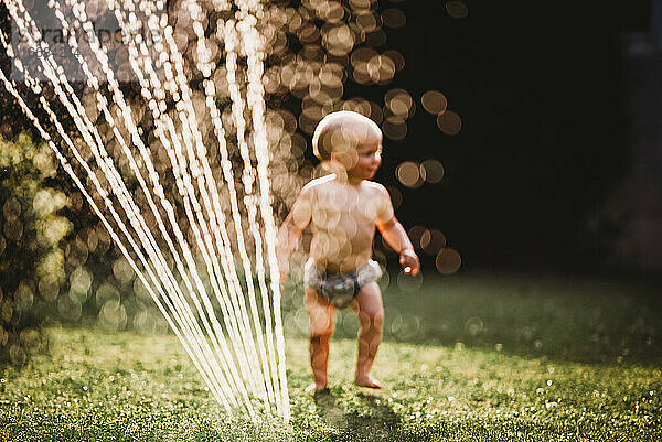 Bokeh Baby im Garten spielen mit Wasser aus Sprinkler
