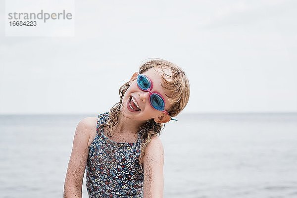 junges Mädchen lachend mit Schwimmbrille beim Spielen am Strand