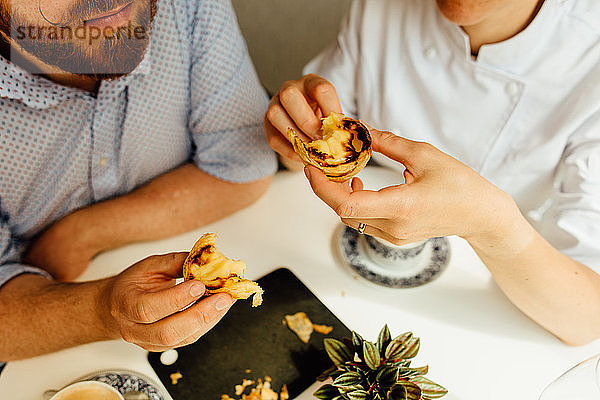 Hände eines Paares beim Verzehr eines Desserts  einer portugiesischen Puddingtorte