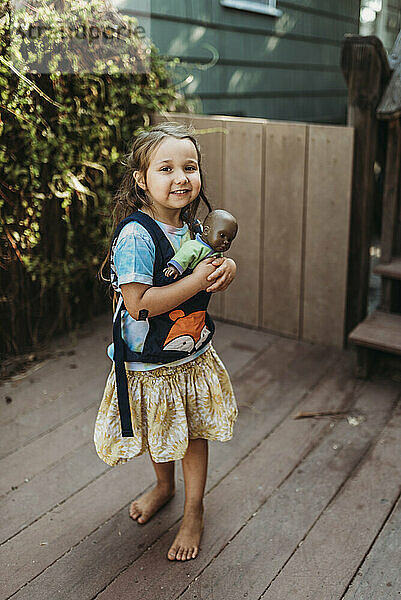 Kleines Mädchen trägt Babydoll in Babytrage draußen im Hof