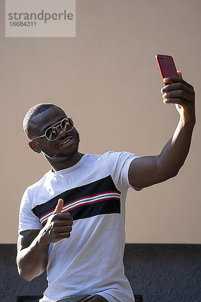 Mann mit Sonnenbrille  der ein Mobiltelefon benutzt.