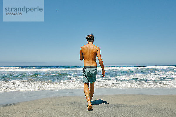 Junger Mann spaziert ohne Hemd zum Pazifik am Strand von Baja  Mexiko.