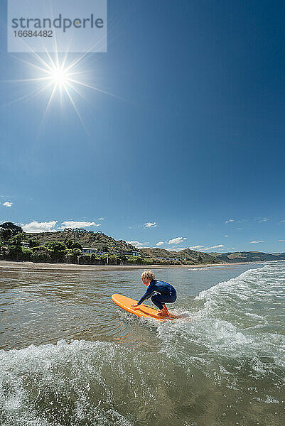 Kleines Kind beim Surfen in Neuseeland an einem sonnigen Tag