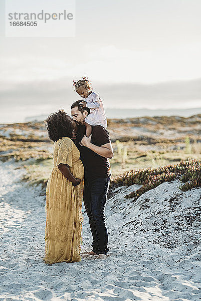 Gesamtansicht einer Familie  die sich bei Sonnenuntergang am Strand küsst