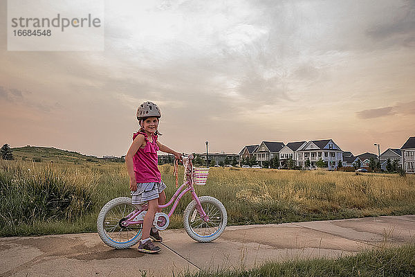 Porträt eines lächelnden jungen Mädchens auf ihrem Fahrrad in einem Park bei Sonnenuntergang