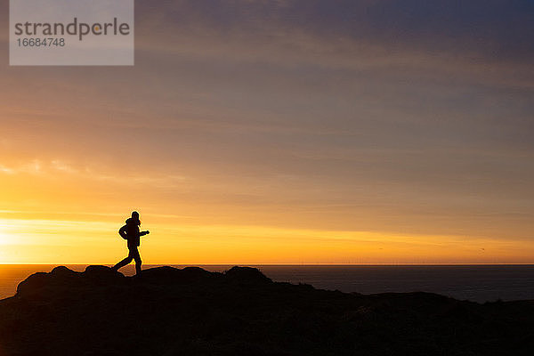 Silhouette einer Frau  die in der Morgendämmerung über das Meer läuft