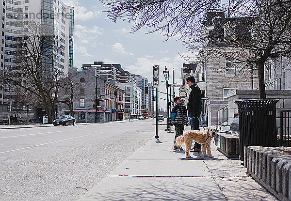 Vater und Sohn mit Hund stehen auf dem Bürgersteig einer ruhigen Stadtstraße.
