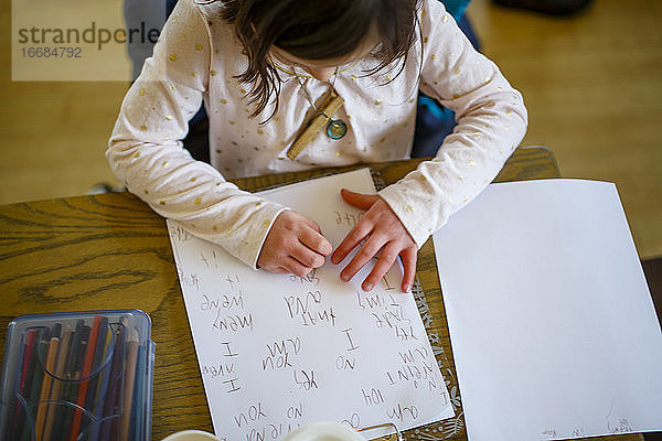 Draufsicht auf ein kleines Kind  das an einem Tisch sitzt und eine Geschichte schreibt