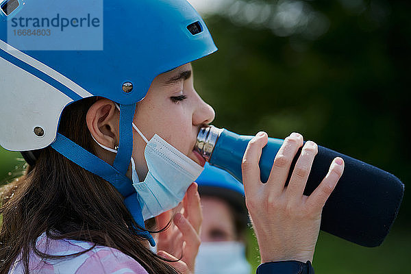 Mädchen mit der Maske und dem Reithelm trinkt Wasser aus einer Flasche