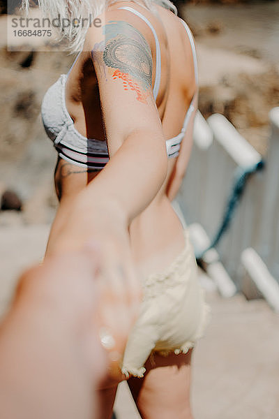 Ein Paar geht am Strand Hand in Hand spazieren. Perspektive vom Arm des Mannes aus