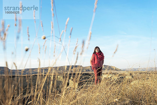 Vorderansicht einer Frau mit Kopftuch  die auf dem Gipfel einer Wüstenschlucht sitzt und zum Horizont blickt