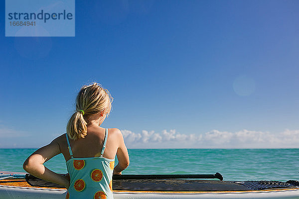 Junges Mädchen mit Paddleboard schaut auf ruhigen türkisfarbenen Ozean
