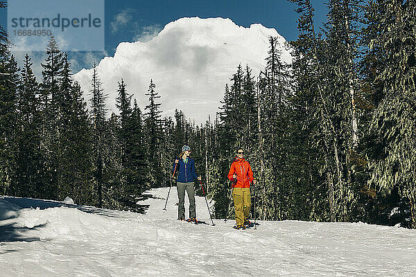 Zwei junge Frauen gehen an einem sonnigen Tag Schneeschuhe auf dem Mt. Hood.