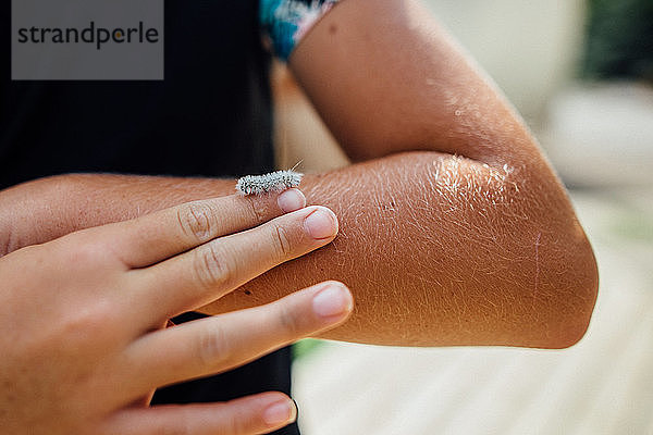 Winzige weiße und pelzige Raupe  die auf dem Finger eines Mädchens herumkrabbelt