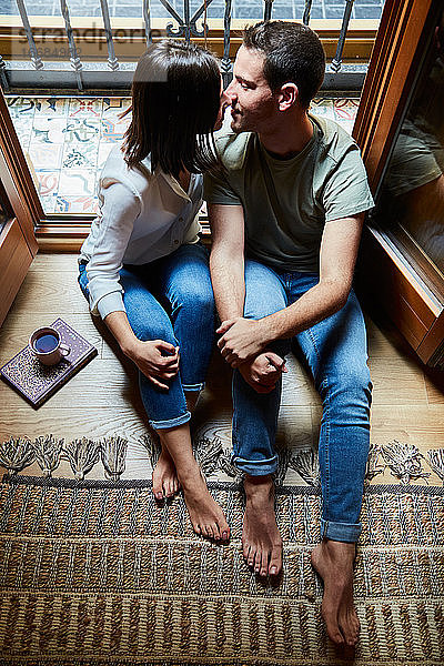 Draufsicht auf ein junges  intimes Paar  das sich zu Hause neben einem Fenster mit Balkon küsst.