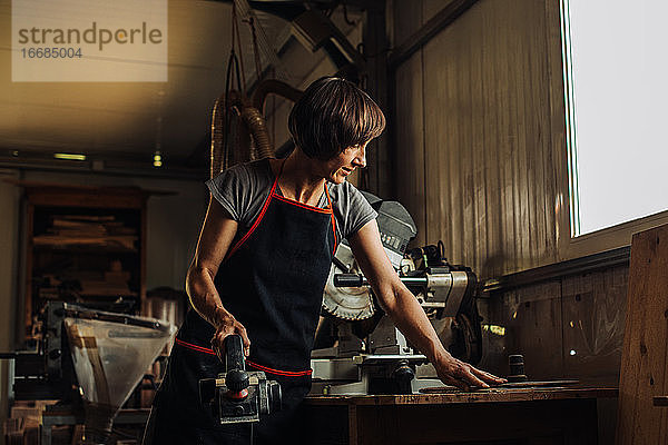 Frau mittleren Alters mit Hobelmaschine in einer Holzwerkstatt