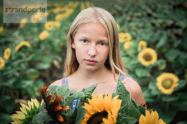 Ernstes junges Mädchen hält Sonnenblumen mit Sonnenblumen im Hintergrund