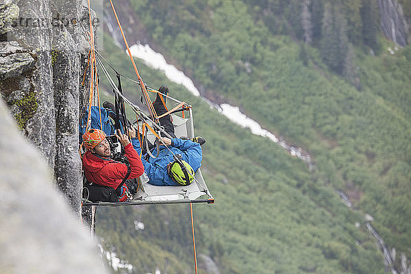 Porträt von Bergsteigern  die während einer Klettertour ein Portaledge benutzen.