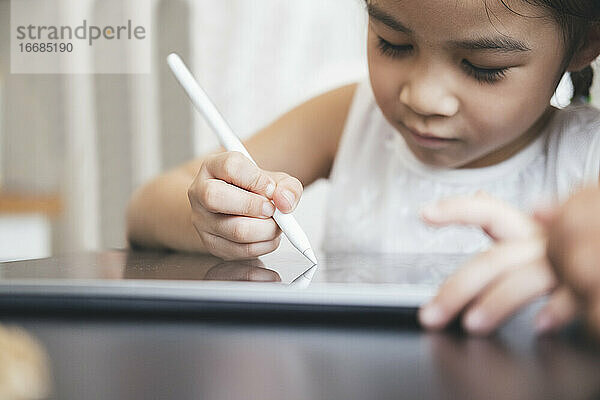 Kleines Mädchen mit Tablet und Stift lernt online zeichnen