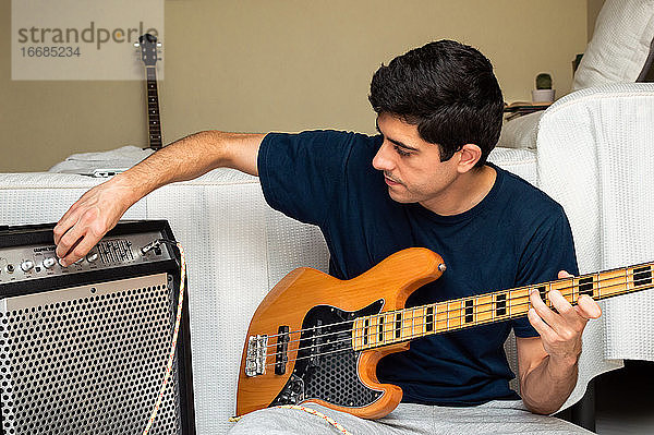 Mann stellt Verstärker ein  um E-Bass zu spielen  während er zu Hause sitzt.