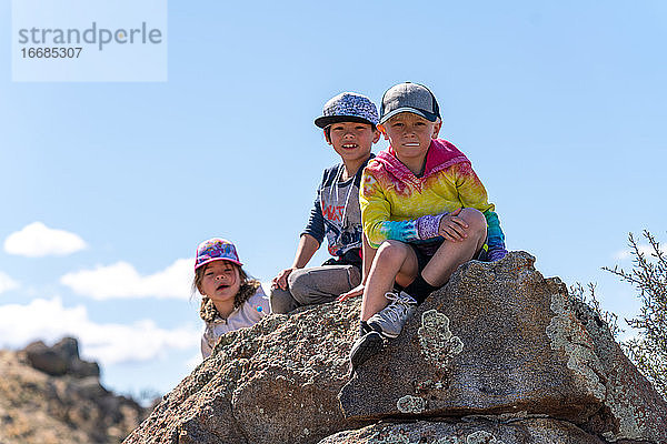 Kinder sitzen auf einem Felsen und schauen in die Kamera