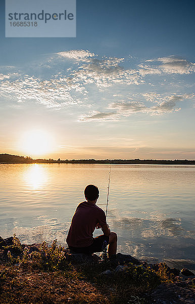 Heranwachsender Junge beim Angeln am Ufer eines Sees bei Sonnenuntergang in Ontario  Kanada.
