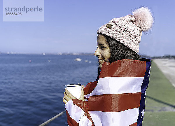 Schöne junge Frau stehend in der amerikanischen Flagge mit einer Tasse eingewickelt