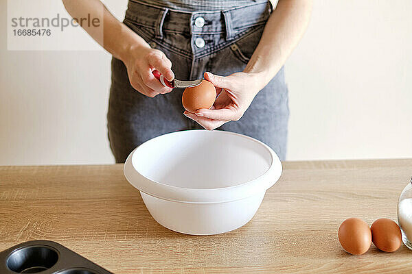 Frau bricht ein Ei mit einem Messer über einem Teller auf  um eine köstliche Mahlzeit zuzubereiten
