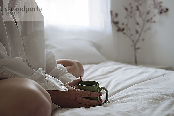 Nahaufnahme von Frauenhänden  die eine Tasse Kaffee auf dem Bett halten.