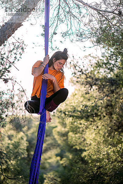 Junges Mädchen  Akrobatin. Übt Seiltanz in der Luft. Frau macht Zirkuskunststücke mit Kleidern im Wald. Sie ruht sich nach dem Training auf dem Band aus.