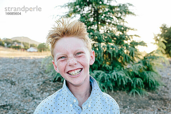 Ein rothaariger Junge mit Sommersprossen lächelt ein verrücktes Lächeln