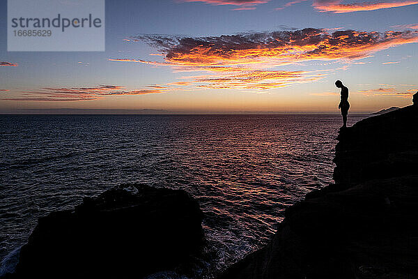 Klippenspringer bereitet sich auf einen Sprung ins Meer bei Sonnenuntergang in Hawaii vor